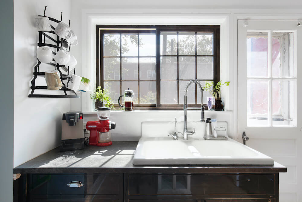 Large enamel sink with granite counter and black lower cabinets and view of french door and large window after renovation