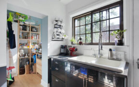 Large white enamel sink with black lower cabinets and view of dry pantry with wooden flooring after renovation