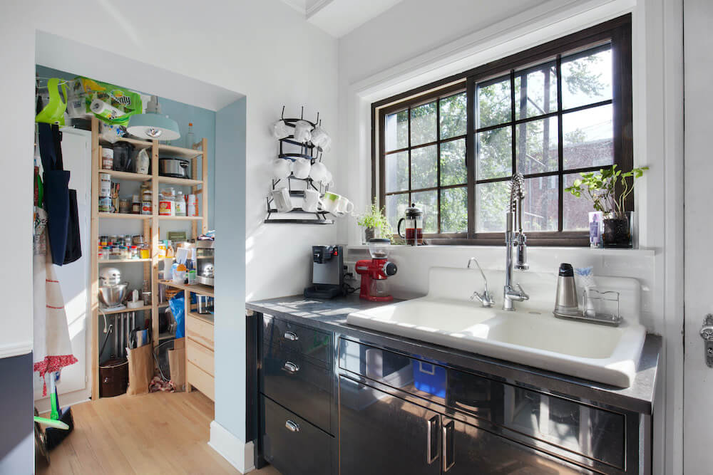 Large white enamel sink with black lower cabinets and view of dry pantry with wooden flooring after renovation