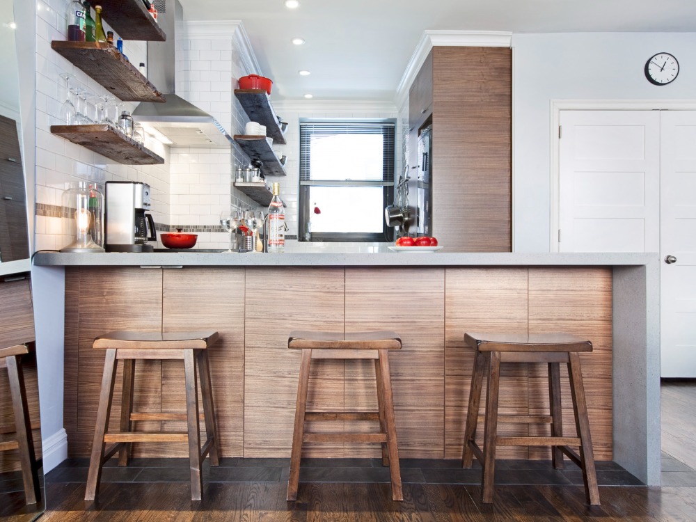 Small brown and white kitchen with concrete peninsula alongside open shelves and bar seating after renovation 