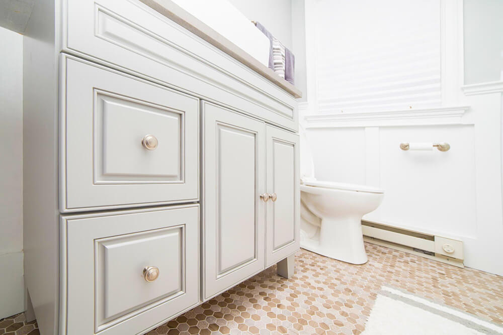 Gray vanity with golden knobs in a white and gray bathroom with toilet after renovation