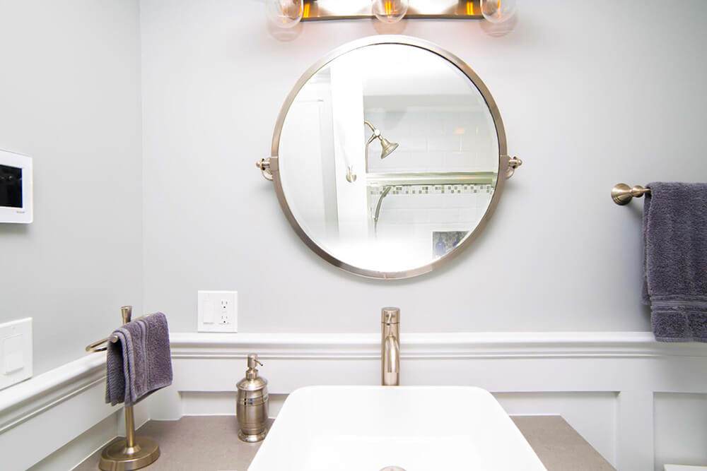 Gold round vanity mirror over white sink and golden nickel finish bathroom fixtures after renovation