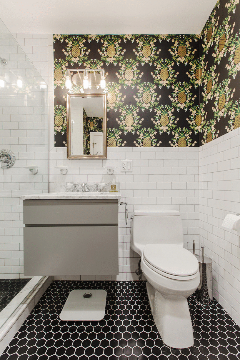 patterned hexagon black floor tiles and a gray vanity in a bthroom with white subway tiles after renovation