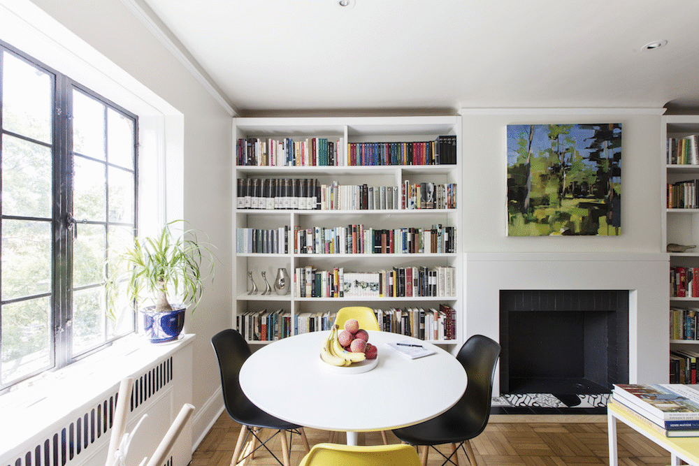 white open book shelf near large window and breakfast nook with white round table and brown wooden floor after renovation