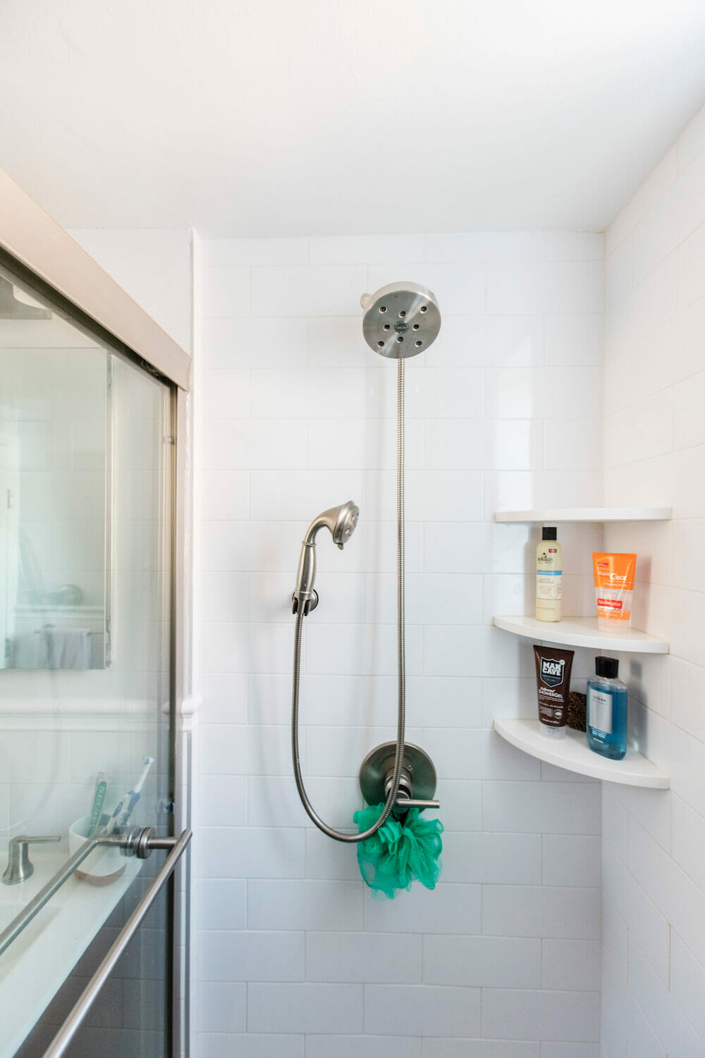 Large nickel showerhead and open shelves in a white walk in shower area with subway tiles after renovation