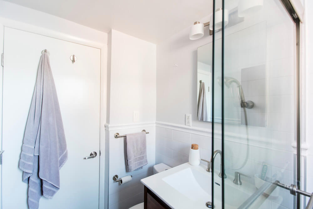 Glass doors for walk in shower in a small white bathroom with white sink and wooden floating vanity after renovation 