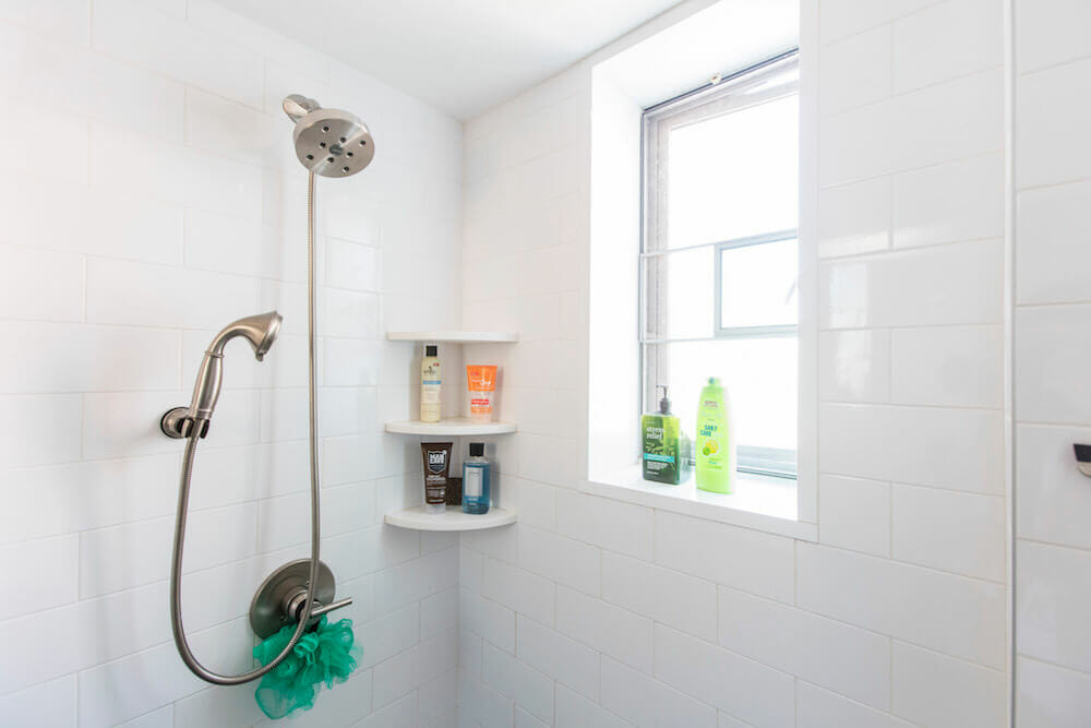 White walk in shower area with large nickel shower head and large window after renovation