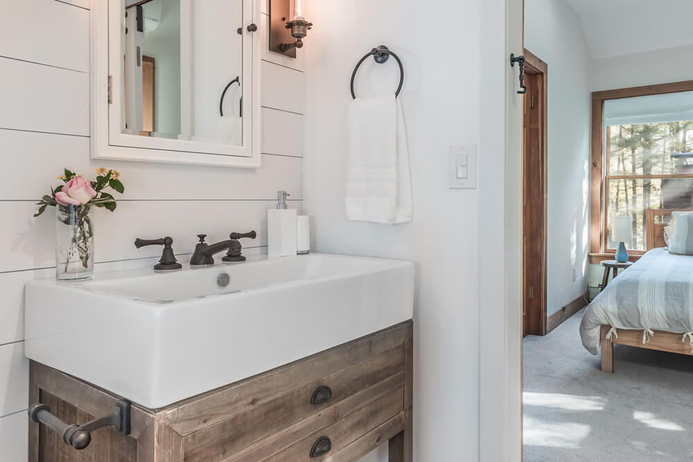 Large white farmhouse sink over wooden vanity in white bathroom space over vanity mirror after renovation