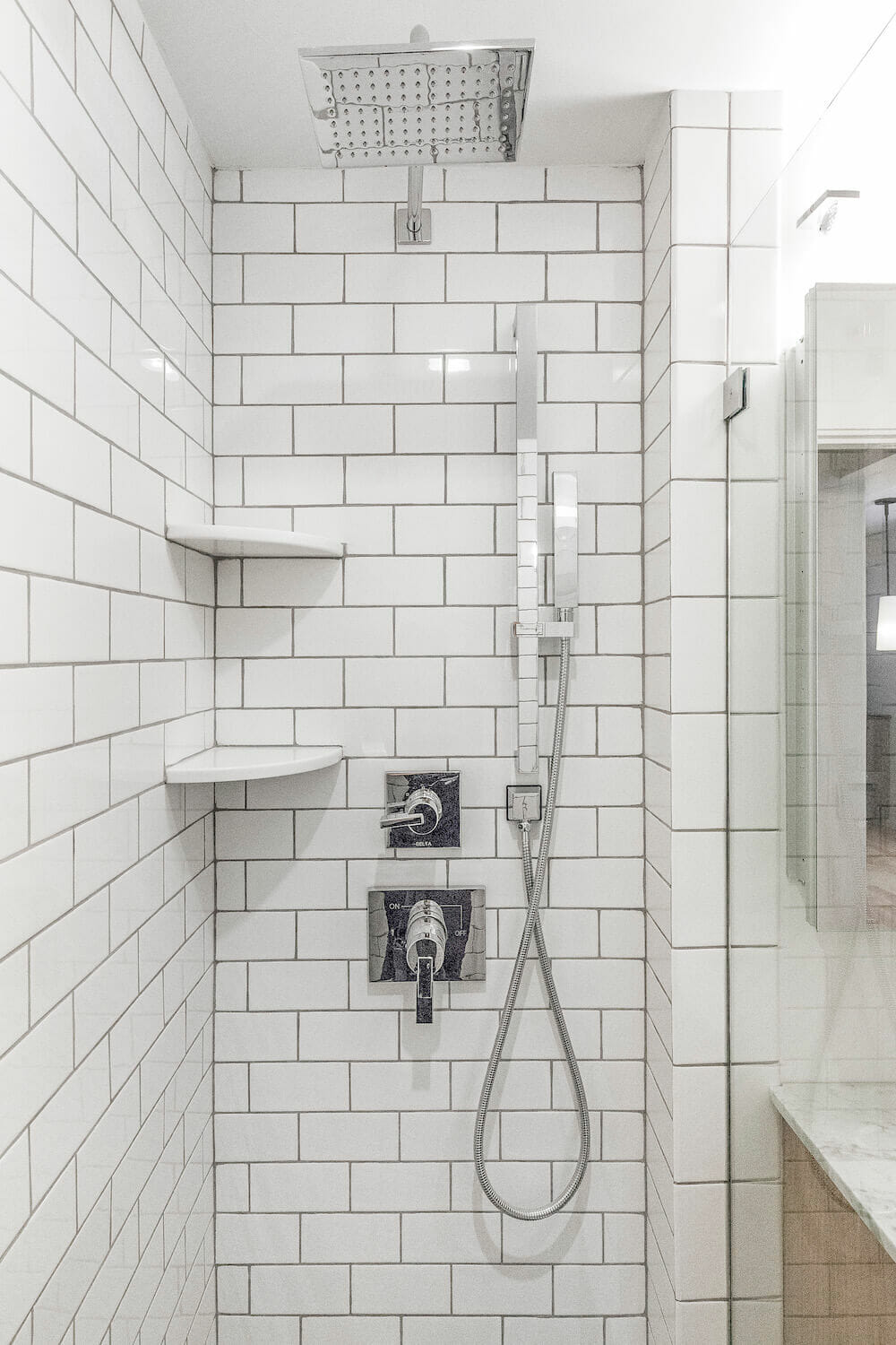 White subway tiles in narrow walk in shower with glass door and an oversized showerhead after renovation