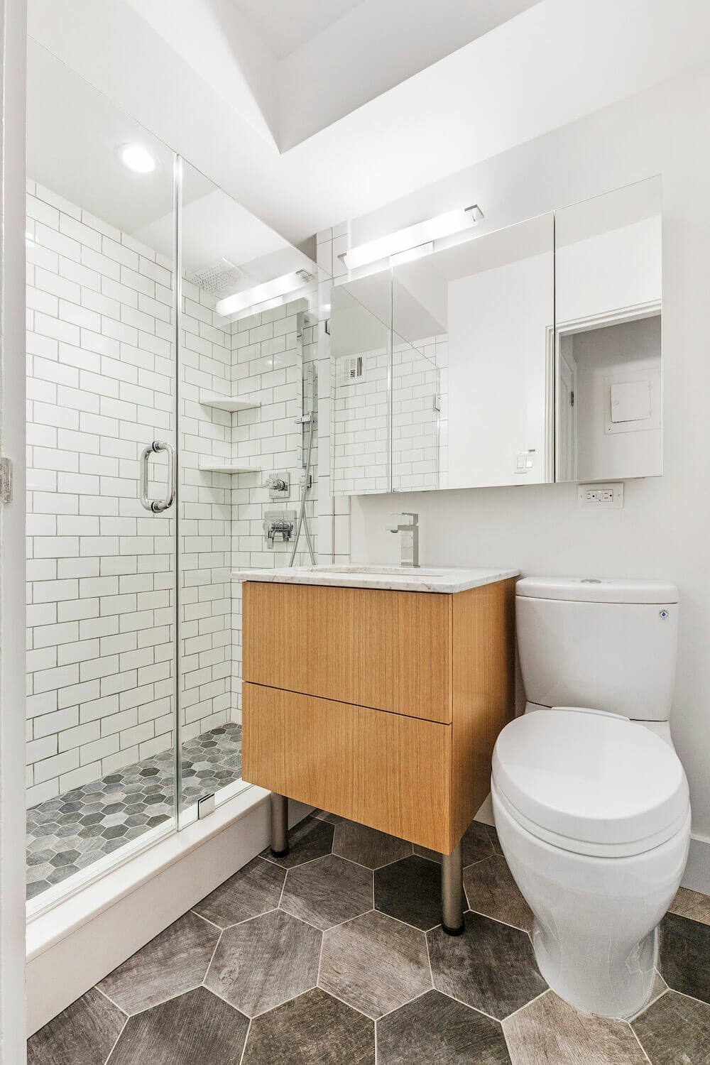 White bathroom with white subway tiles and contrasting gray grouting with slate colored hex tiles in shower and bathroom after renovation