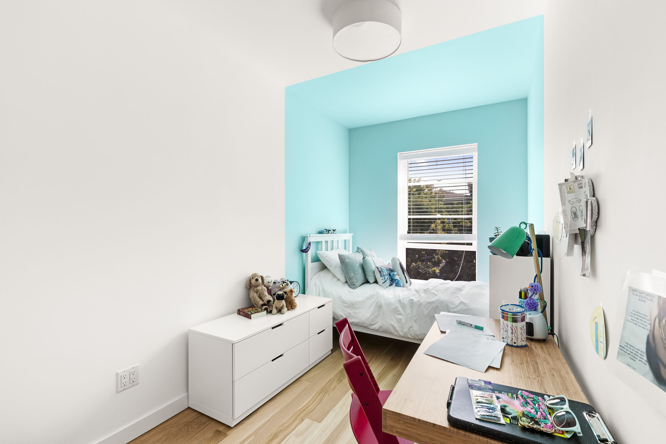White Oak Wood Flooring warms a Bedford-Stuyvesant bedroom with a turquoise sleeping nook, white walls, low storage, and a child’s study desk.