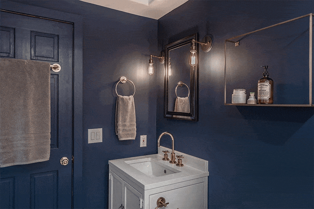 Blue bathroom with white sink and vanity and black vanity mirror after renovation