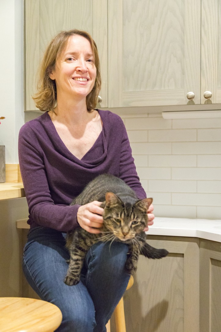 proud homeowner with cat in gray kitchen with white backsplash after renovation