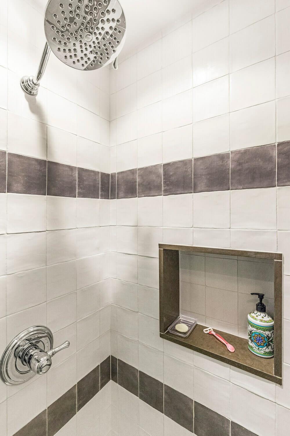 Large nickel showerhead in a white bathroom with dark gray trim after renovation