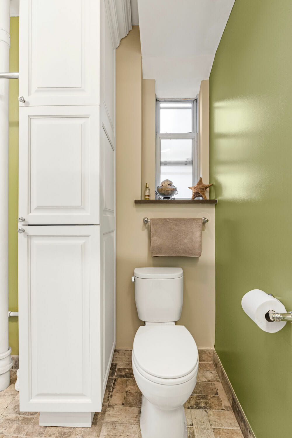 White toilet near green wall and white storage cabinetry after renovation