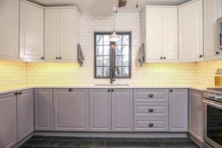 gray kitchen cabinets in a kitchen with white subway tiles and white overhead cabinets after renovation