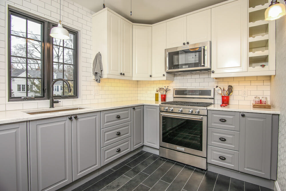 gray kitchen cabinets under white countertop and white overhead cabinets in a kitchen with black framed glass panelled window after renovation