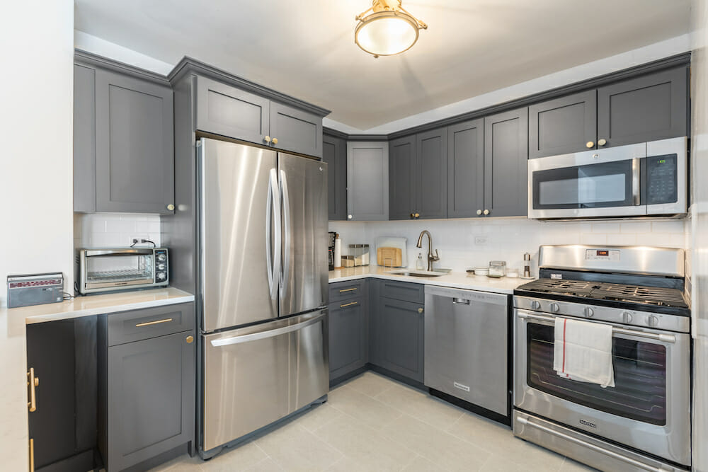 gray kitchen cabinets and silver appliances in a small kitchen with hanging pendant light after renovation