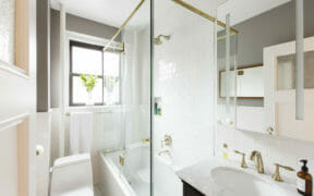 frameless glass enclosure for white bathtub in a white bathroom with white oval sink after renovation
