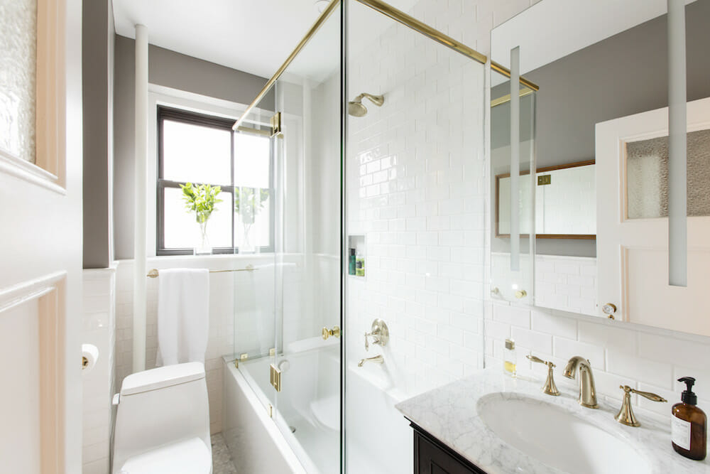 frameless glass enclosure for white bathtub in a white bathroom with white oval sink after renovation