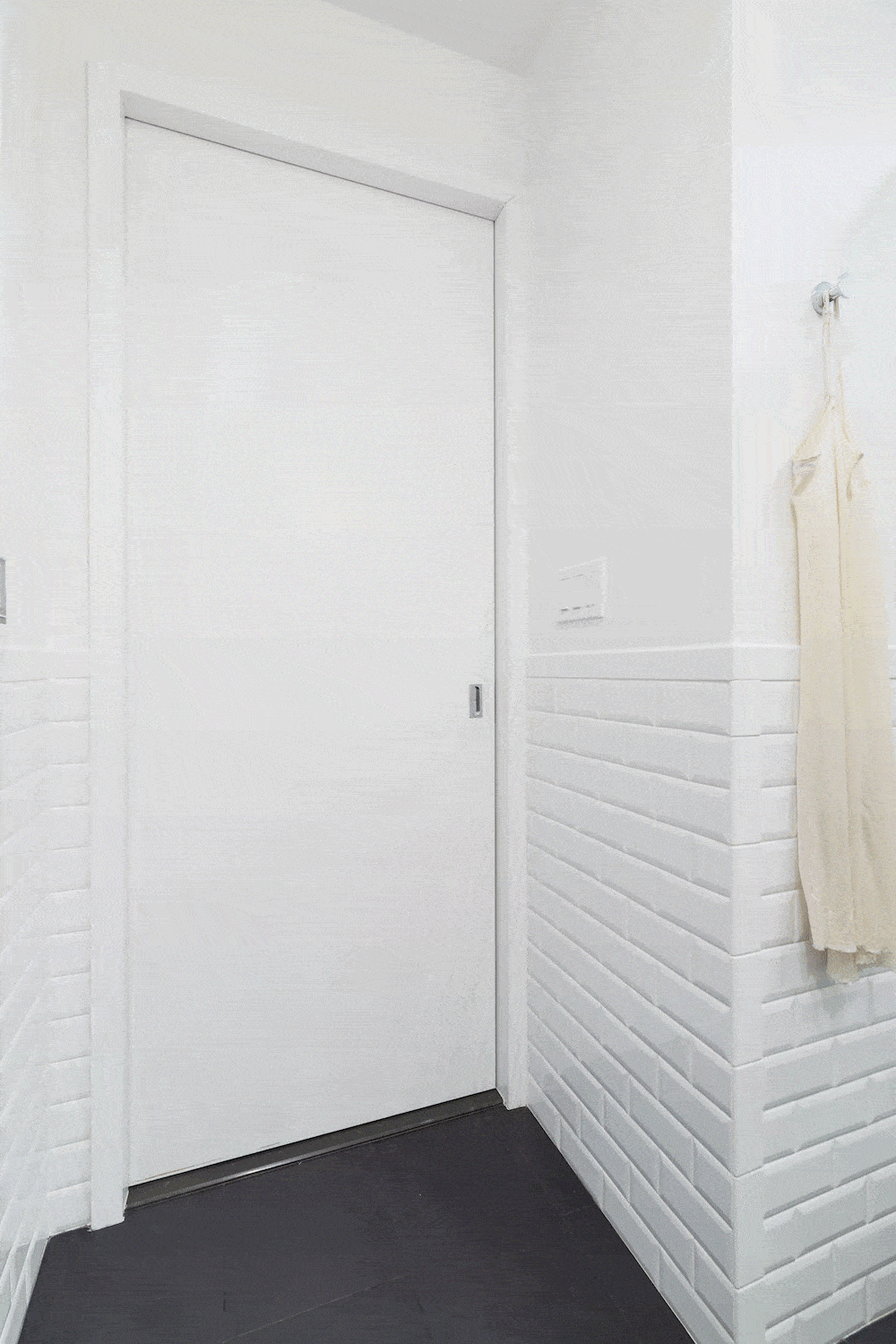 White bathroom with white door and dark floor tiles after renovation