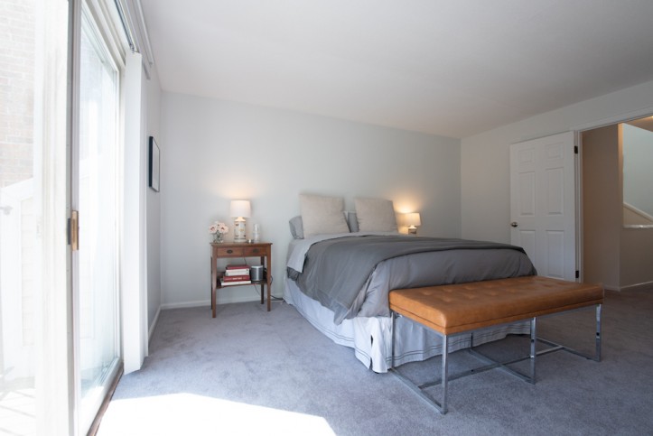 white bedroom with bed and bedroom bench on a gray carpeted floor after renovation