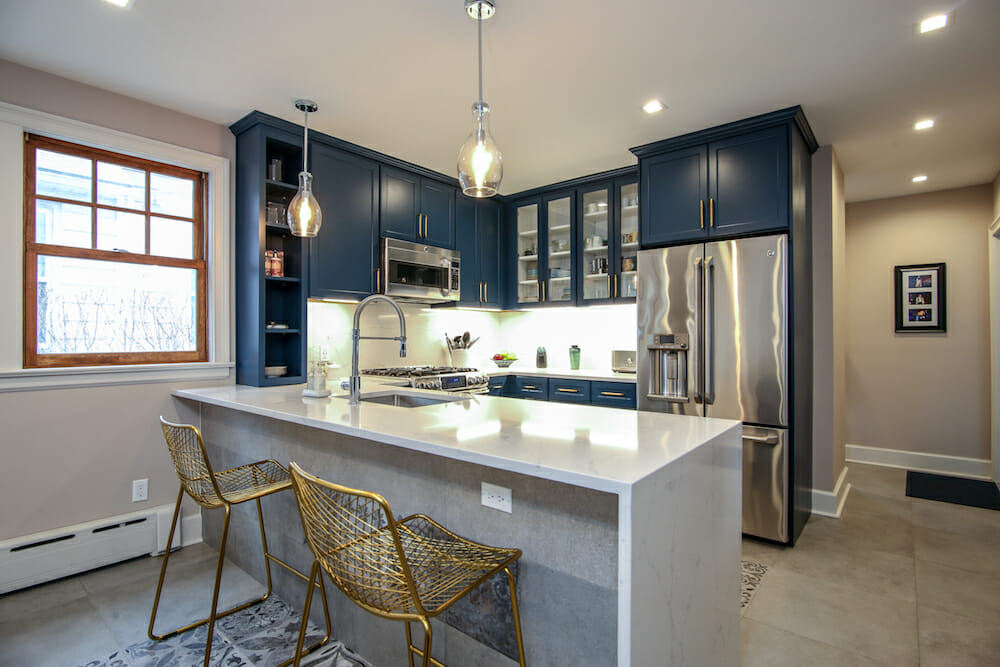 white kitchen peninsula with golden chairs and blue kitchen cabinets with silver appliances after renovation 