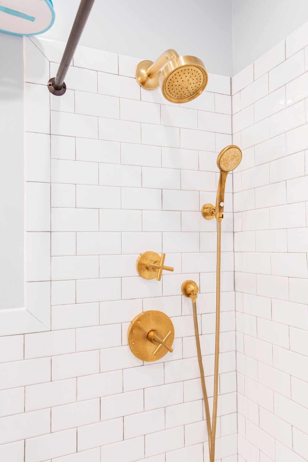 White shower area with white subway tiles and bright gold bathroom fittings after renovation