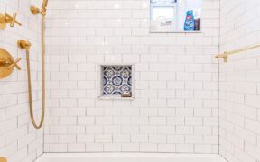 White subway tiles in shower area with bright gold bathroom fittings and recessed shower shelf after renovation