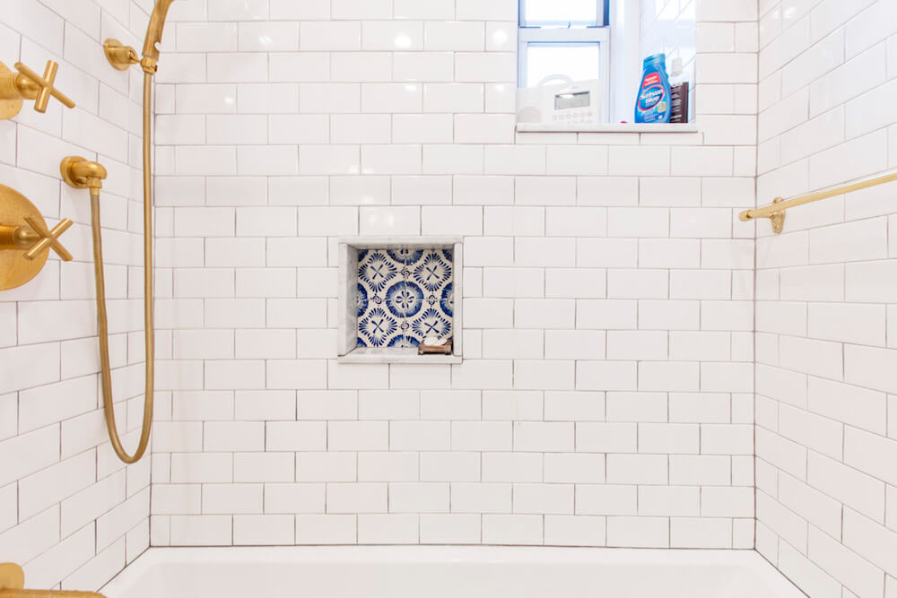 White subway tiles in shower area with bright gold bathroom fittings and recessed shower shelf after renovation