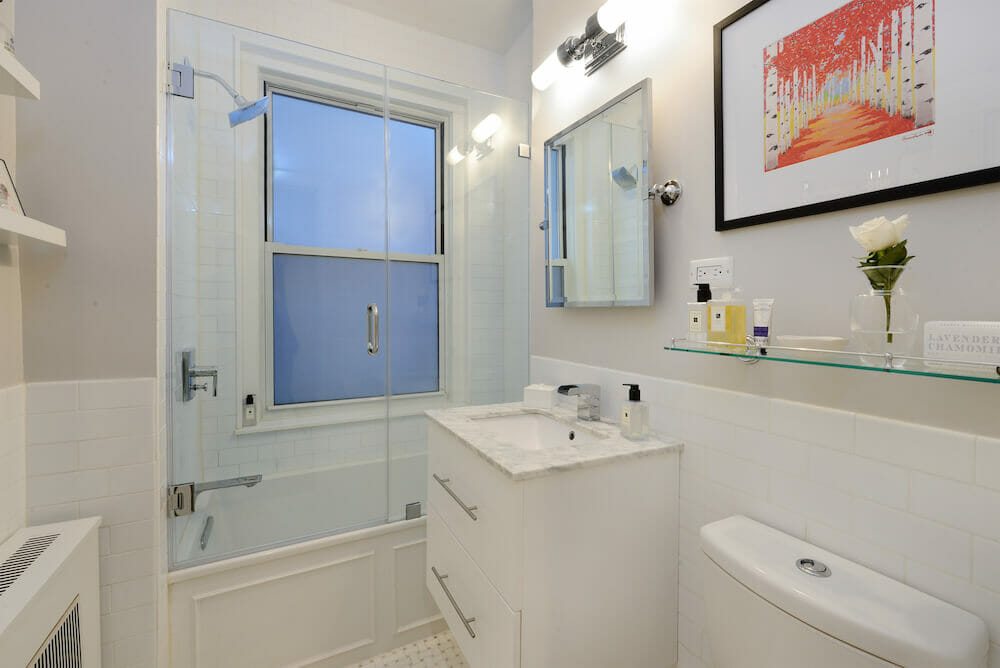 White bathroom with white floating vanity and sink alongside glass doors for walk in shower after renovation