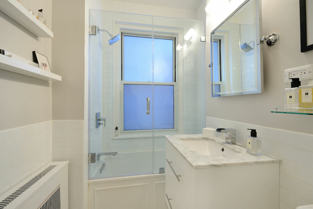 White and gray bathroom with blue double hung window near the shower niche and white vanity after renovation