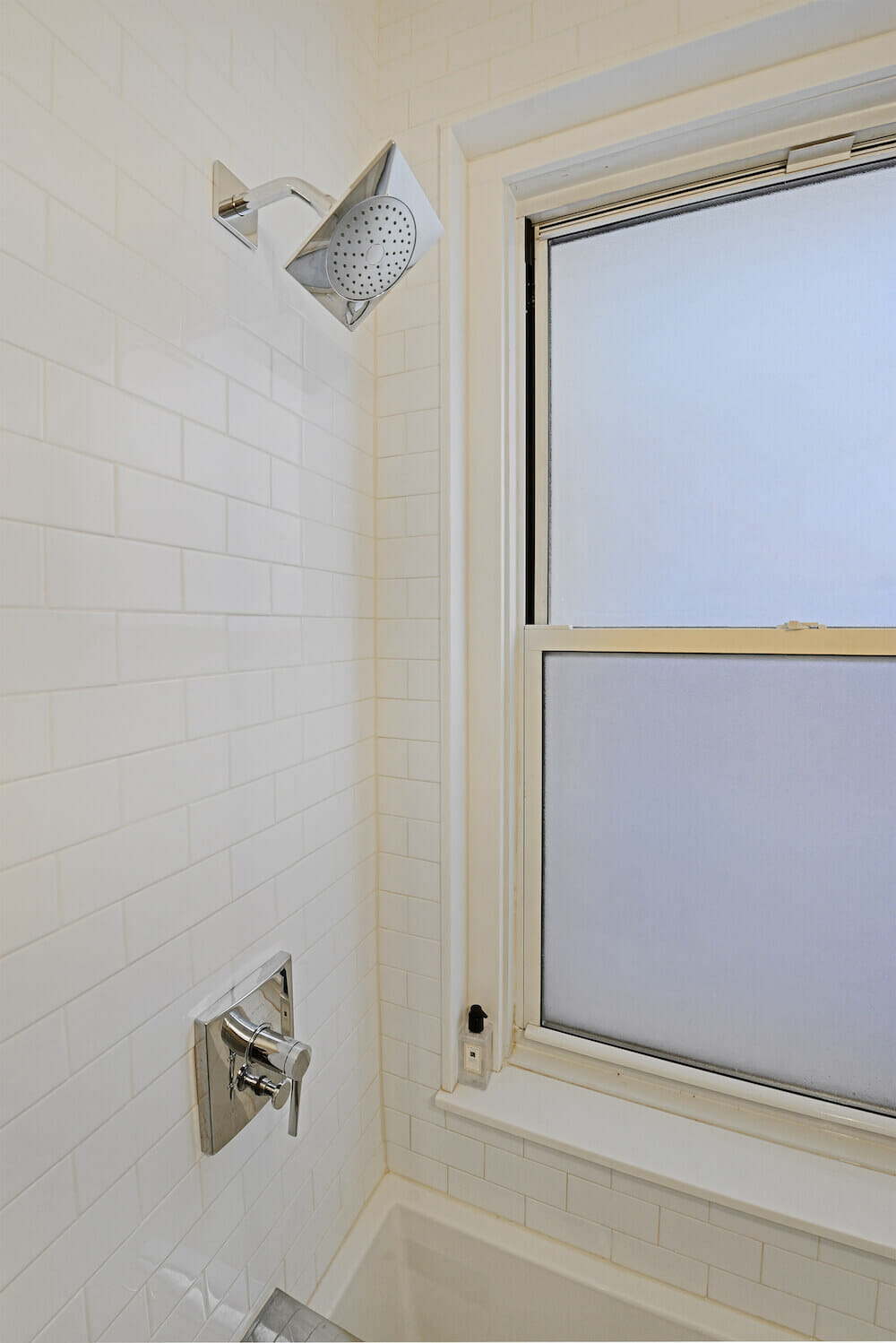 White bathroom with subway tiles and double hung mirror on window ledge and nickel coated showerhead after renovation