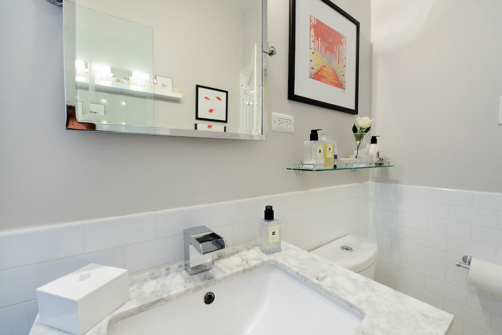 White bathroom with half white subway tiles and marble countertop for a white sink and large vanity mirror after renovation
