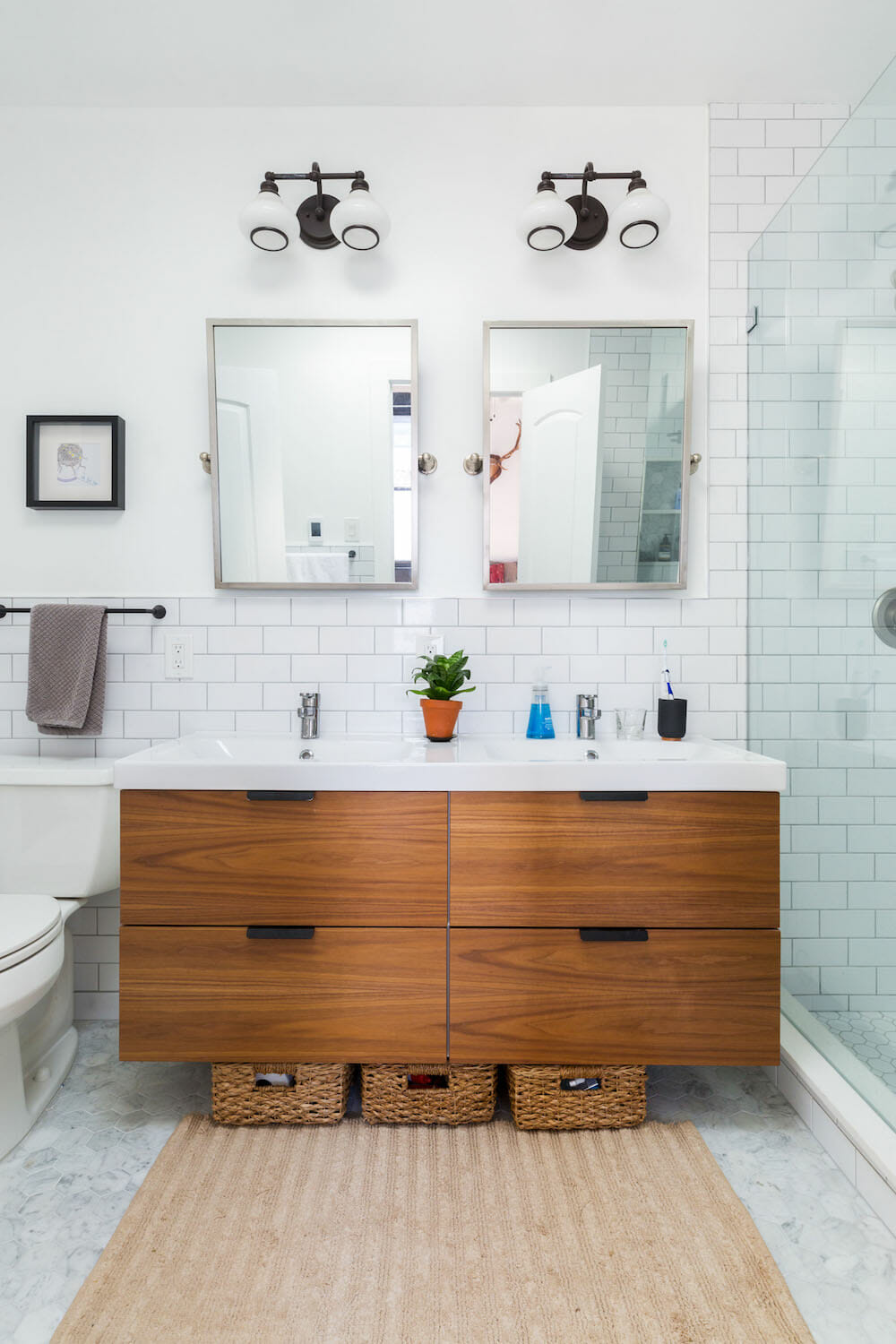 white bathroom with white subway tiles and brown floating vanity with double white sinks after renovation 