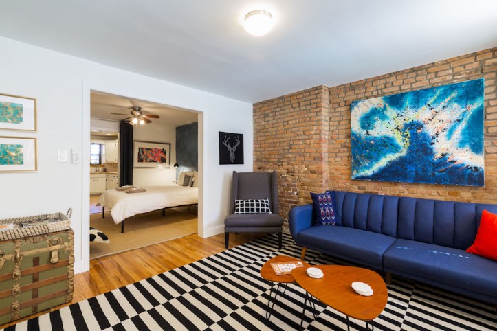 brick wall with a blue couch over black and white rug and a chest of drawers after renovation
