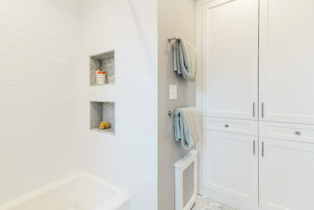 White bathroom with recessed shower shelf and white storage cabinets after renovation