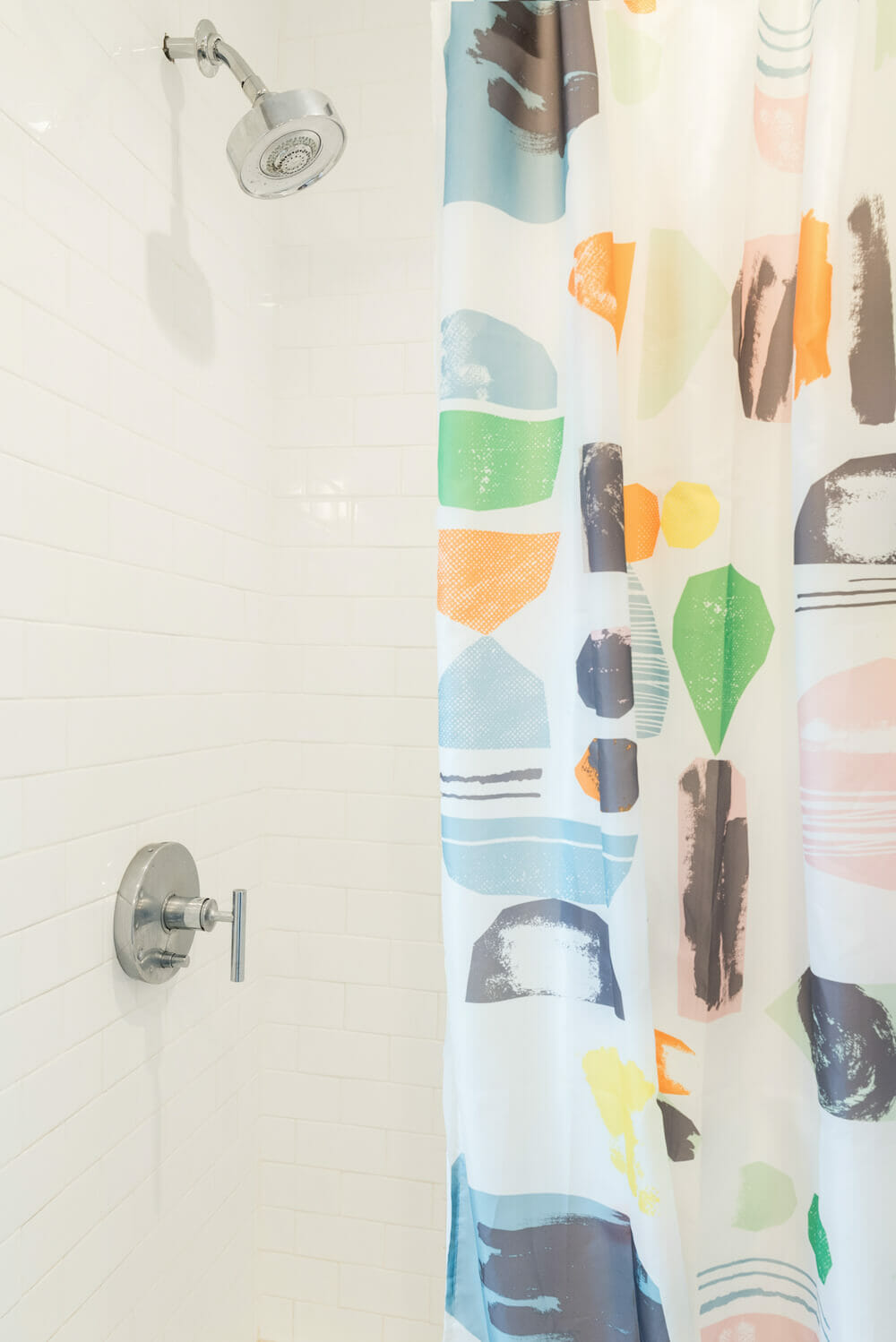 White bathroom with subway tiles and nickel bathroom fittings and colorful shower curtain