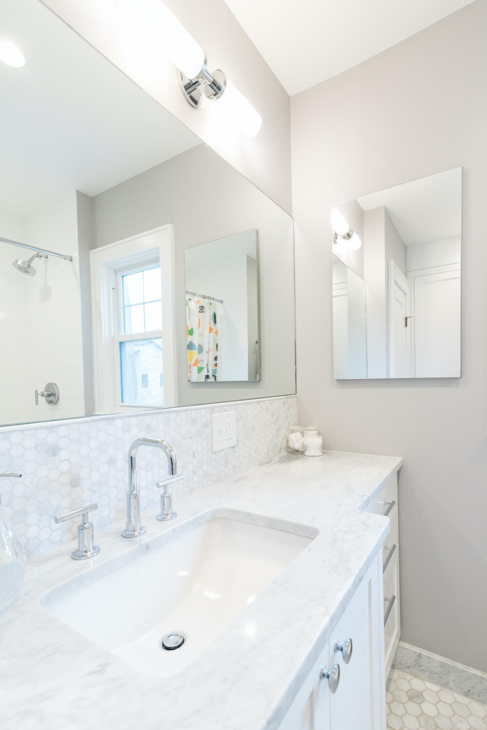 Large white sink with white marble countertop and large vanity mirror below light fixtures after renovation 