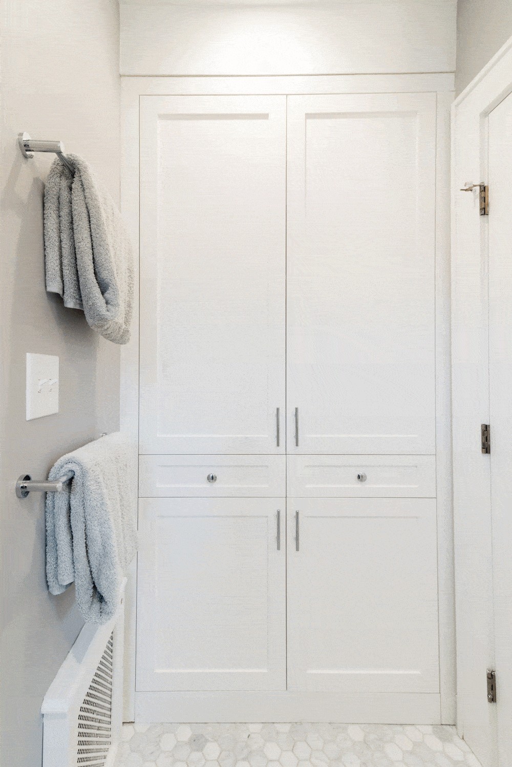 Large white linen closet and gray wall with towel hangers in the bathroom after renovation