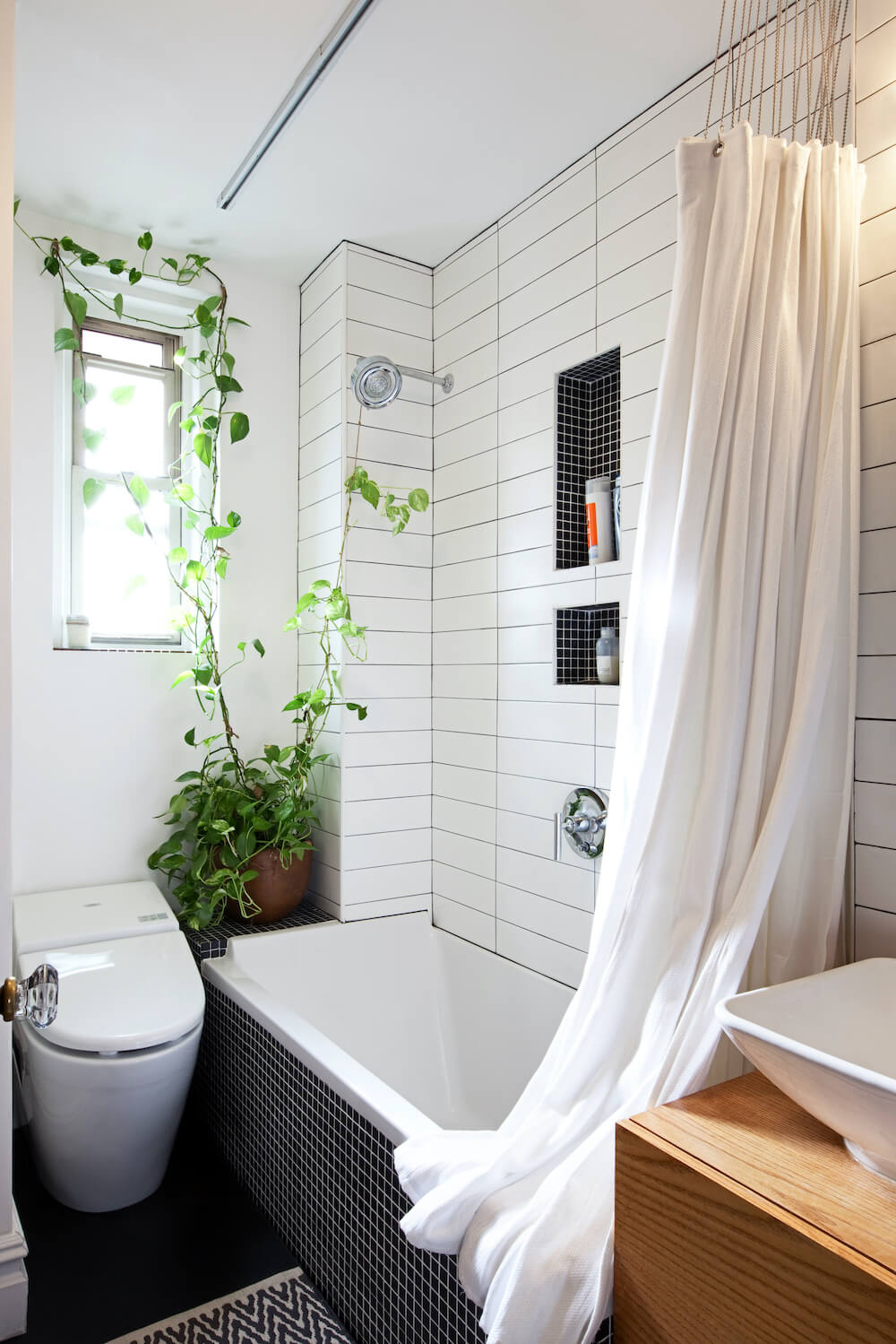 White bathroom with white tub covered by a shower curtain and white toilet and black floor tiles after renovation