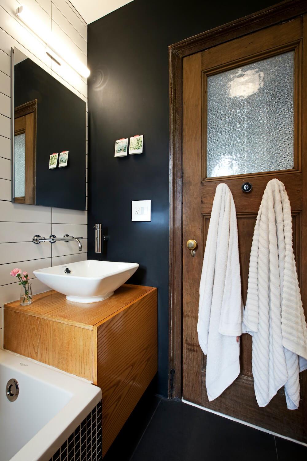 Black and white bathroom with brown door near white sink and wooden vanity after renovation