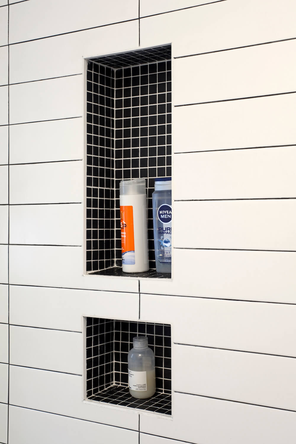 White bathroom tiles with gray grouting and recessed shower shelf with black mosiac tiles after renovation