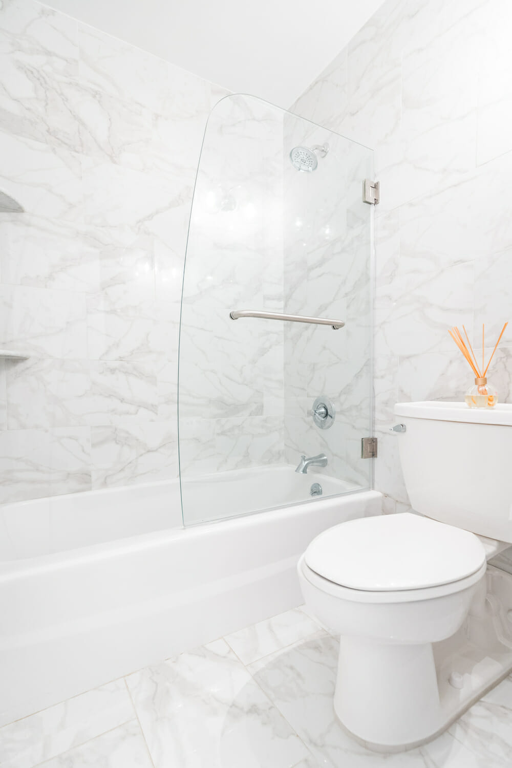 calacatta marble wall in a white bathroom with glass separator and a bathtub after renovation