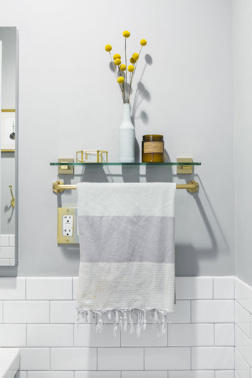 gray bathroom wall with white subway tiles and open glass shelf and towel hanger after renovation
