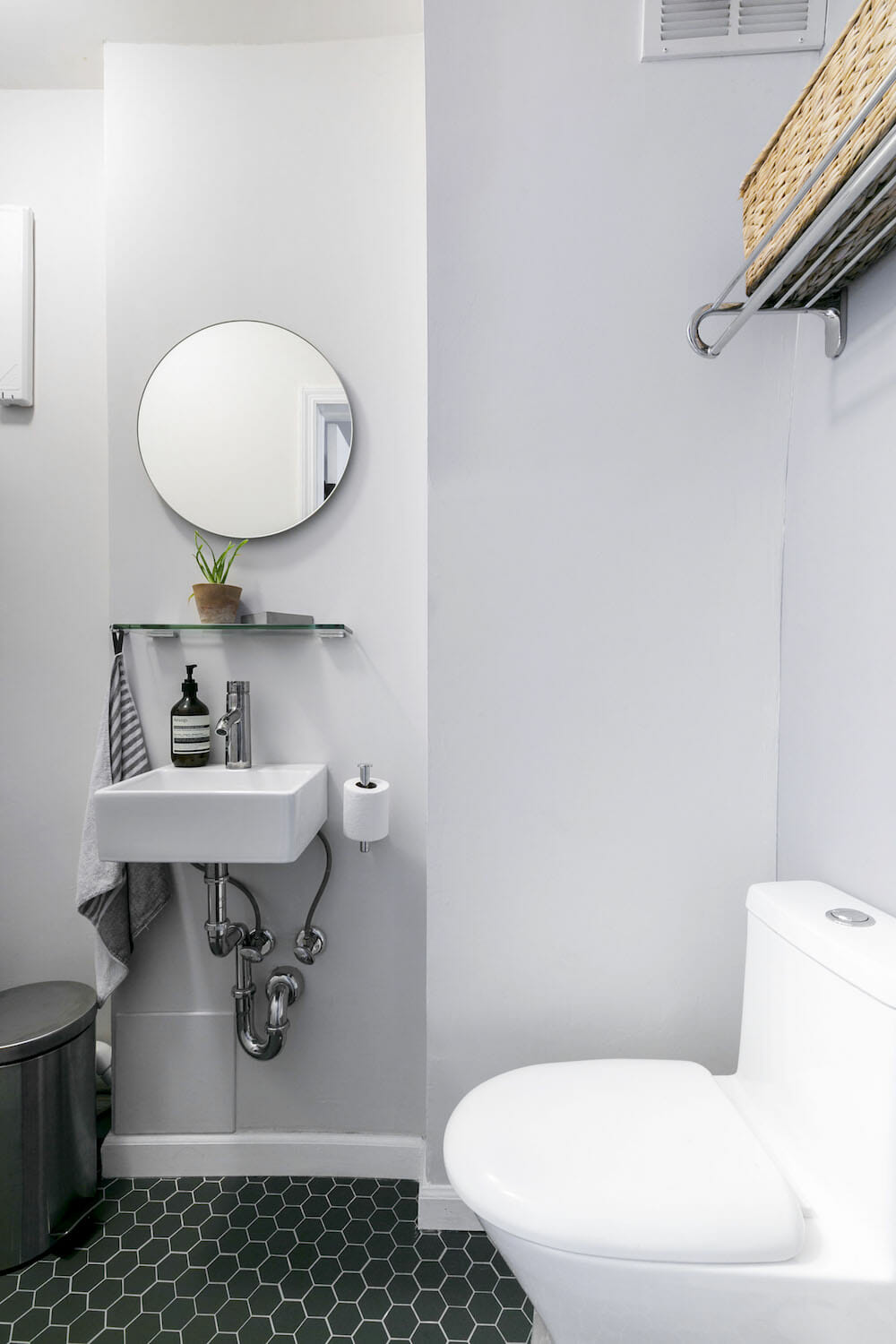 gray powder room with white sink and round vanity mirror and overhead towel hanger after renovation