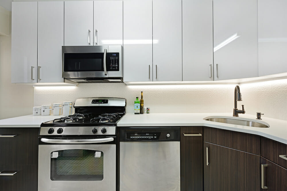 Glossy white upper cabinets over white countertop and white backspash along with under cabinet lighting after renovation