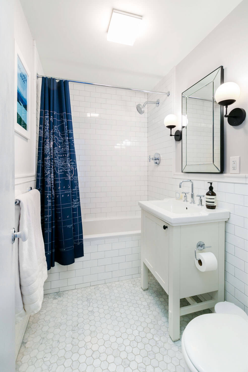 White subway tiles on wall with hex tiles on floor along with large mirror and vanity after renovation