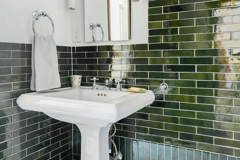 Dark green wall tiles with pedestal sink and bathroom mirror after renovation
