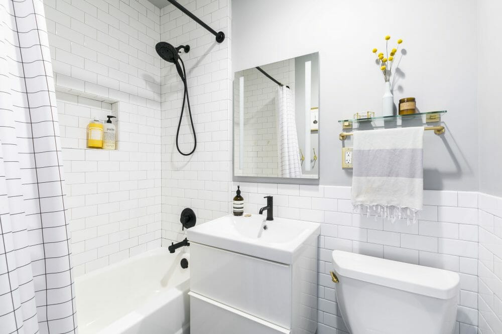 bathroom with white subway tiles and bathtub and black fixtures and white vanity and toilet after renovation